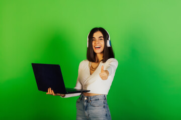 Happy student girl in headphones holding laptop and showing thumb up. Cool day. 