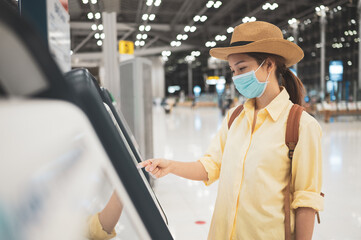 Asian woman wearing face mask  self checking-in printing a boarding pass at the airport while coronavirus pandemic concept of Safety travel under COVID-19 speading