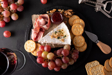 piece of brie cheese with grapes, crackers and red wine
