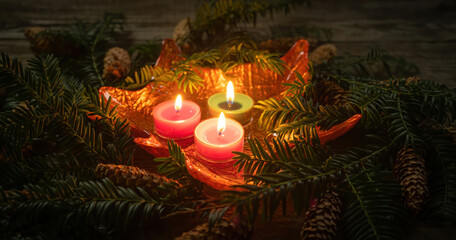 Christmas decoration with burning candles on dark background with branch with needles. Close-up and shallow depth of field. Christmas holidays and New Year theme