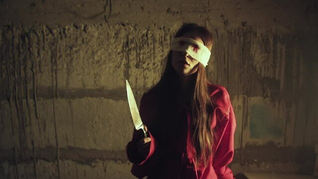 Scary killer girl in red clothes with a knife and bloody eyes. Halloween costume. Blood on the bandage on the eyes. The knife in the hands of the killer