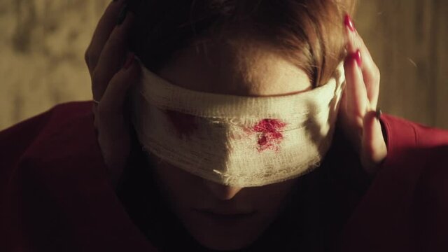 A scary girl in red clothes with a bloody bandage over her eyes. Blind woman with no eyes with halloween mask