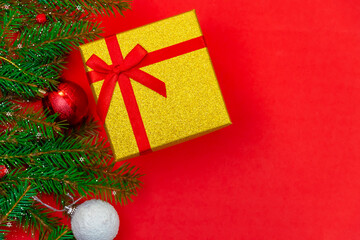Gift box with a red bow, spruce branch and Christmas balls with snow and lights on a red background close up with copy space, top view. Christmas or New Year background.