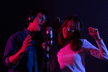 Young Asian man and woman singing to condenser microphone in studio. Professional vocalist wearing...