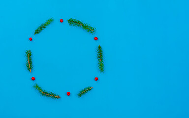 Circle of Christmas tree branches, Rowan berries on a blue background with copy space, top view. Minimal Christmas holiday concept. Christmas background