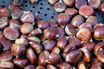 Fall and winter rustic dessert sweet roasted chestnuts in a large metallic bowl, available for sale at a street food market festival, seasonal food photograph with selective focus.