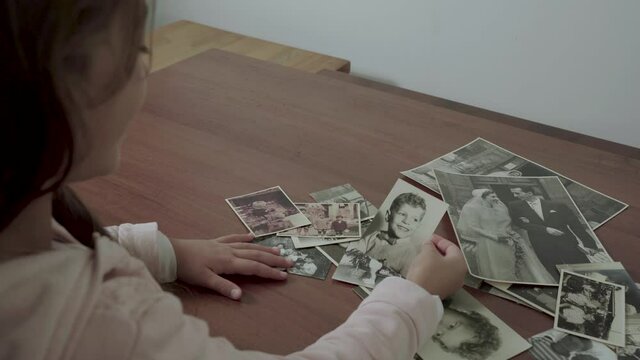 Female child is looking at old photos of her family with grandfather, grandmother and father when they were young FDV