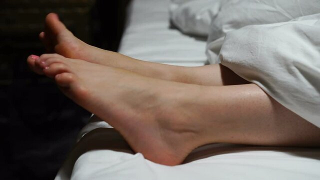 Woman's feet sticking out of blanket on bed at home