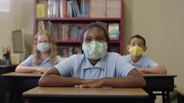 Young students wear masks and listen in class then black girl raises her hand