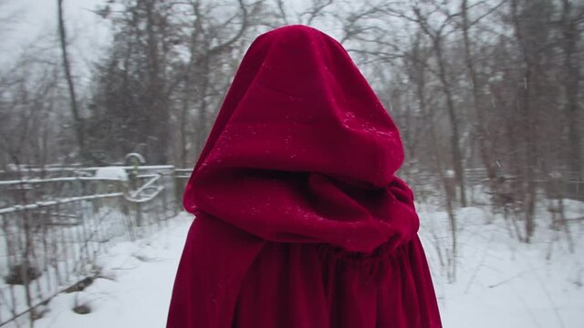 Little Red Riding Hood walks through the snowy cemetery alone. A girl in a red hooded cloak with a terrible scary pattern on her face. Skeleton mouth. image for halloween
