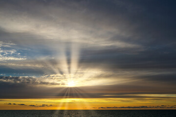 The sun shines through multilayer clouds. Sunset over the sea. The sun peeps out from behind the clouds at sunset