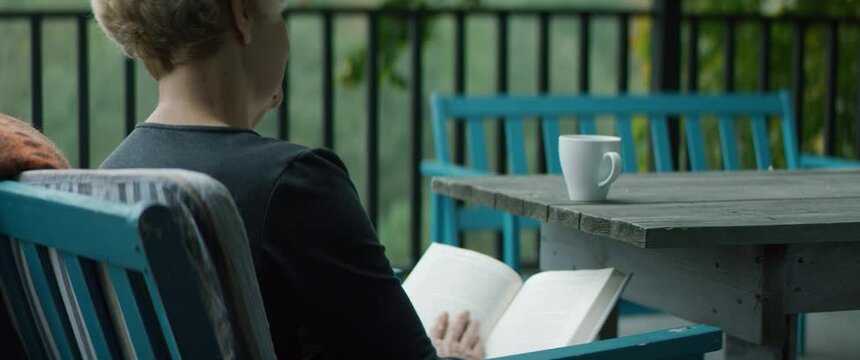 Senior adult mature Caucasian female reading a book on an outdoor terrace of her house on a misty morning. Happy retirement concept. Shot on RED cinema camera with 2x Anamorphic lens