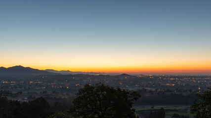 A clear sky lights up during the sunrise over the plain with the last city lights