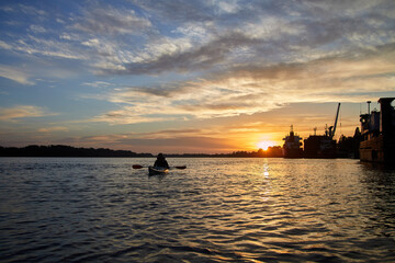 Fototapeta na wymiar Sillouette of man kayaking on the Danube river at sunset near ship