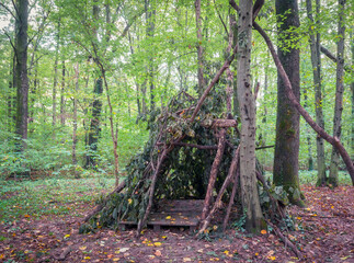 Survival shelter in the woods from tree branches. Cone or pyramid shape shelter.