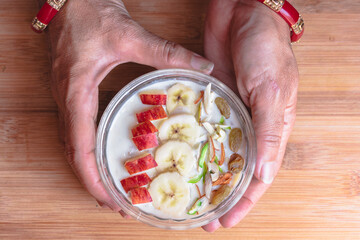 Top view of hands holding Oatmeal bowl garnished with fruits and nuts on wooden table