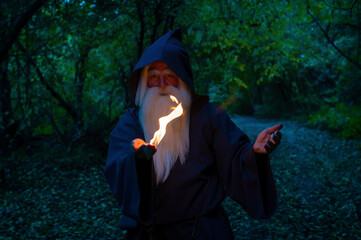 An elderly gray-haired witcher casts a fire spell in the forest. Man in wizard costume
