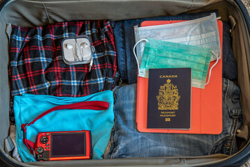 Canadian passport with travel items in suitcase, including masks for coronavirus. 