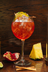 Glass of ice cold Aperol spritz cocktail served in a wine glass with pineapple and garnet, placed...