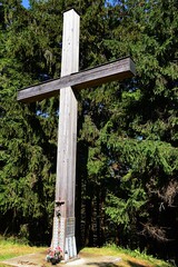 Large wooden cross placed near tourist path on crest of Javorniky mountains, boundary between Czech Republic and Slovakia, sunlit by bright summer sunshine. 