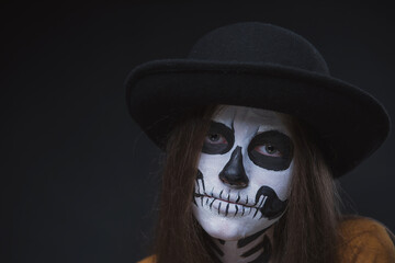 Girl with a skeleton make-up on her face on a dark background with a sad expression