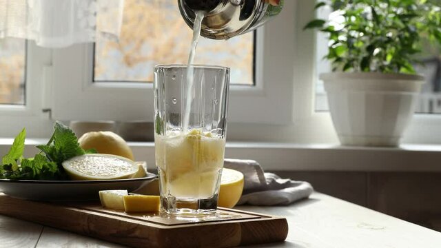 Woman pouring grapefruit gin and tonic cocktail in the glass on the white table near window in the sunny falltime. Selective focus, shallow depth of the field. Alcohol cocktail or detox drink.