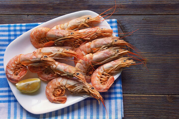 Dish with boiled shrimps and slice of lemon on dark rustic table. Copy space