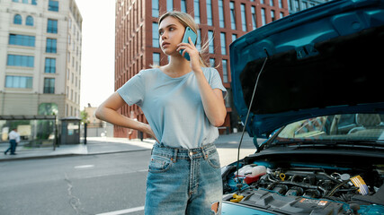 Attractive young woman calling emergency car service, talking on the phone while standing near her...