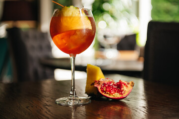 Glass of ice cold Aperol spritz cocktail served in a wine glass with pineapple and garnet, placed...