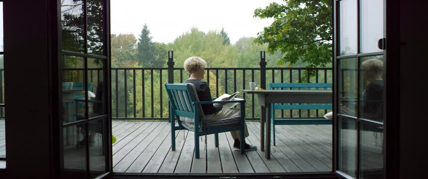 Senior adult mature Caucasian female reading a book on an outdoor terrace of her house on a misty morning. Happy retirement concept. Shot on RED cinema camera with 2x Anamorphic lens