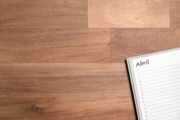 Blank page of a daily planner in Spanish for the month of April on a wooden desk