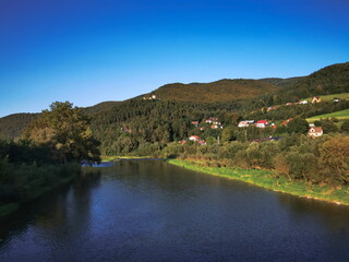 Fototapeta na wymiar The river flows among the autumn Beskid Sadecki mountains. The Poprad river in the town of Rytro.