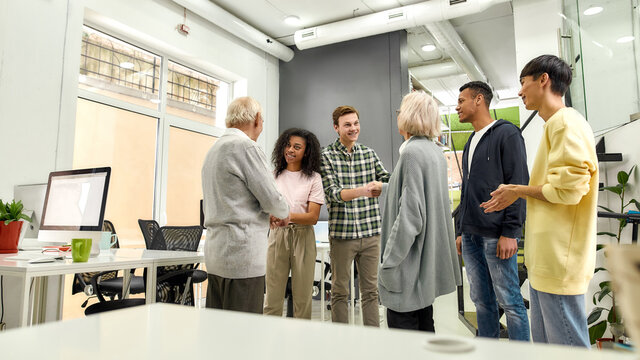 Cheerful young team greeting new employees, Aged man and woman, senior interns shaking hands with colleagues in the modern office