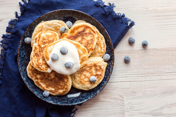 pancakes on a dark blue plate with a blue napkin and blueberries on a light background, top view, soft selective focus