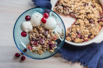 portion of berry crumble with ice cream in a blue glass bowl on a light background, soft selective focus
