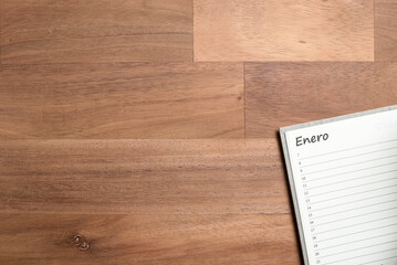 Blank page of an agenda in Spanish for the month of January, on a wooden desk