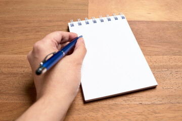 Left hand of a young left-handed woman writing on a blank page of a notebook
