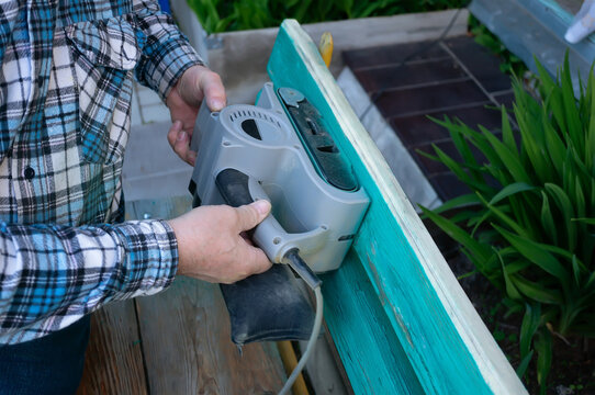 Landscaping of the garden. handyman sharpens a wooden bench on the street in the garden. master removes a layer of dry paint from the wood surface using an electric sander