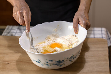 Eggs on raw dough in a bowl mixed with a fork by a woman.