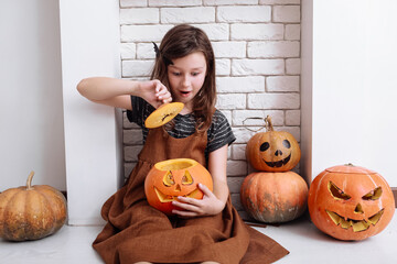 little girl with carving pumpkin on Halloween at home sitting next to fireplace in living room....