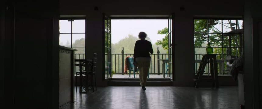 Senior adult mature Caucasian female walking with a cup of coffee and a book to a terrace of his house on a misty morning. Shot on RED cinema camera with 2x Anamorphic lens