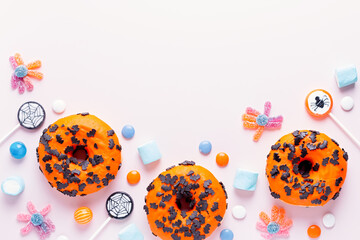 Pumpkin and chocolate donuts, spider lollipops, gummy candy and marshmallows on pink - Halloween...