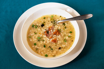 Soup with smoked meat and barley groats in white plate.