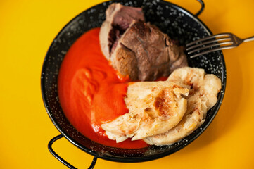 Beef shin, dumplings and spicy tomato sauce in black rural pan on yellow background