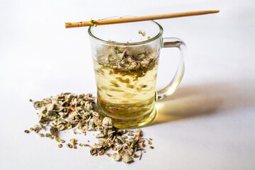 Glass cup of tea in motion, stirrer and pile of Origanum Dictamnus.