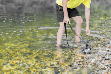 A child stands in the river on outdooor and destroys a mirrorless photo camera. The concept of...