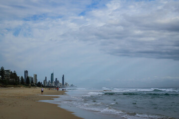 Early morning sunrise at the beach, with cloudy sky and city skyline. Gold Coast, Queensland, Australia. People walking on the sand. 