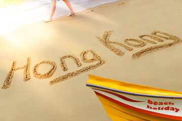 Hong Kong title on the sand beach of the South China sea. The red amber boat stands on the shore. A man walks along the coast.