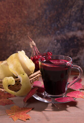 Drink mulled wine in a glass Cup on a dark wooden background with autumn leaves, viburnum berries and apples in a wicker vase. Place for a copy space