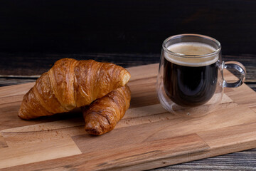 Croissants with a cup of coffee on a wooden board.